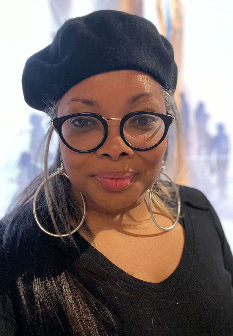 Jennifer Turner, artist and founder of Fine Art of Jenn, smiling and standing in front of one of her unique art pieces.